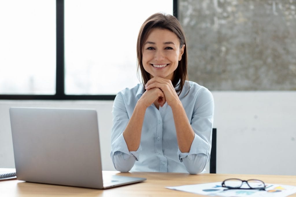 A smiling asian woman sitting at a desk with a laptop.